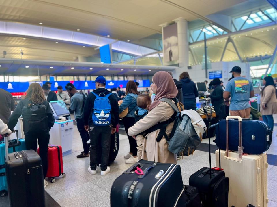 A woman in a hijab holding a baby and standing in line at a Delta kiosk.