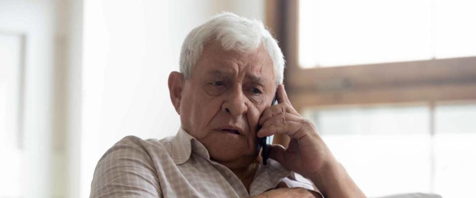 Worried older man sitting on couch, making phone call