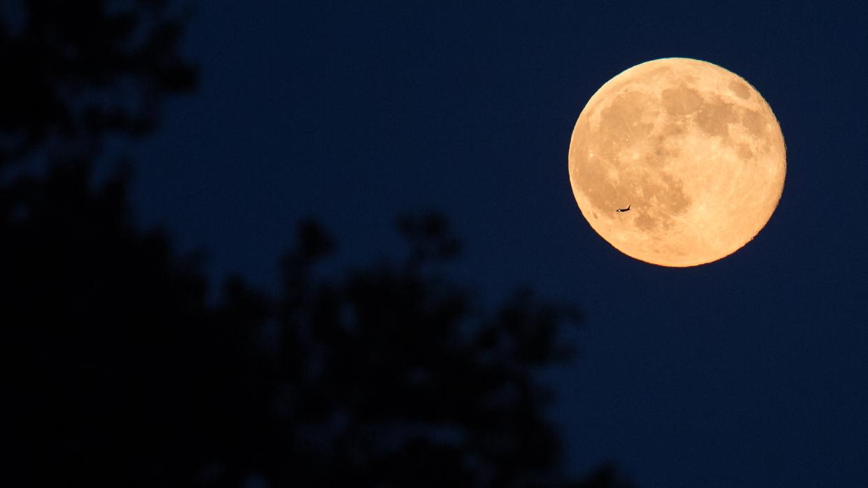  A full moon rises over Arlington, Virginia. A plane passes in front of the moon's bright face. 