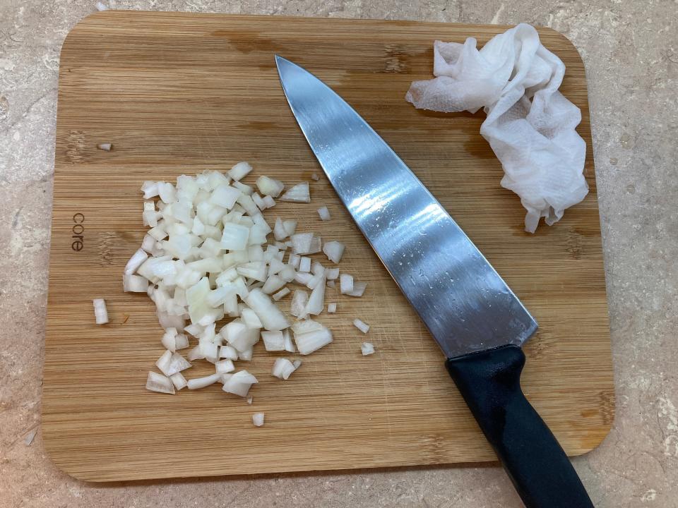 A damp paper towel on a cutting board with diced onions.