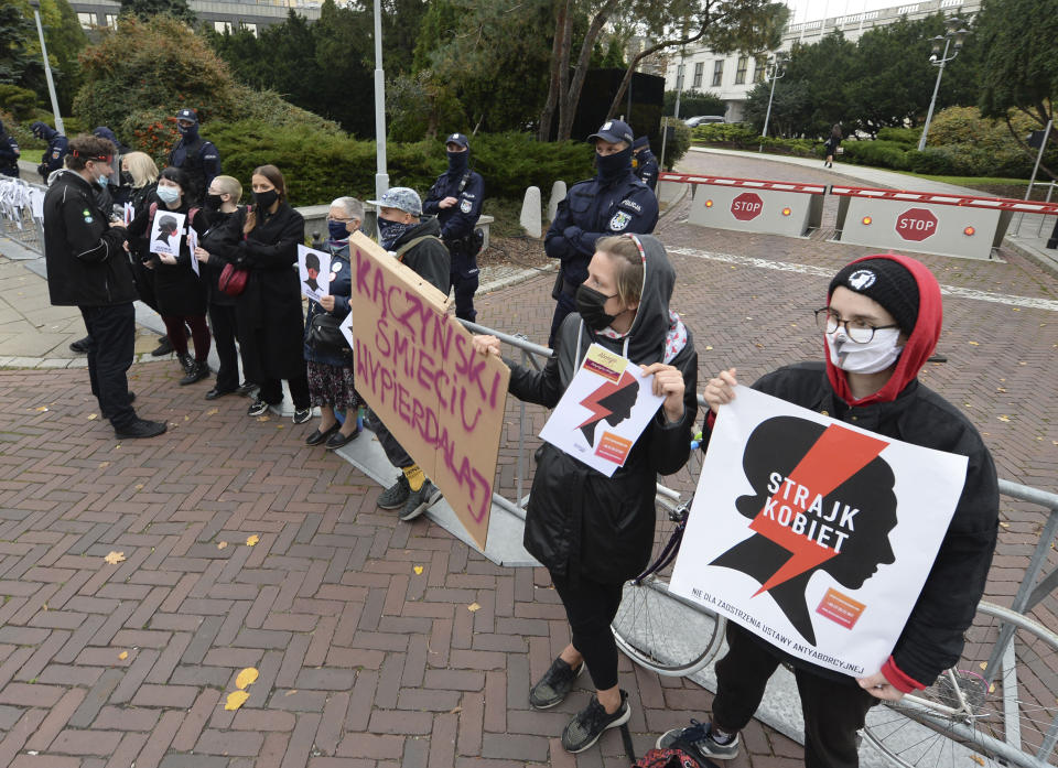 Women's rights activists with posters of the Women's Strike action protest against recent tightening of Poland's restrictive abortion law in front of the parliament building as inside, guards had to be used to shield right-wing ruling party leader Jaroslaw Kaczynski from angry opposition lawmakers, in Warsaw, Poland, on Tuesday, Oct. 27, 2020. Massive nationwide protests have been held ever since a top court ruled Thursday that abortions due to fetal congenital defects are unconstitutional.(AP Photo/Czarek Sokolowski)