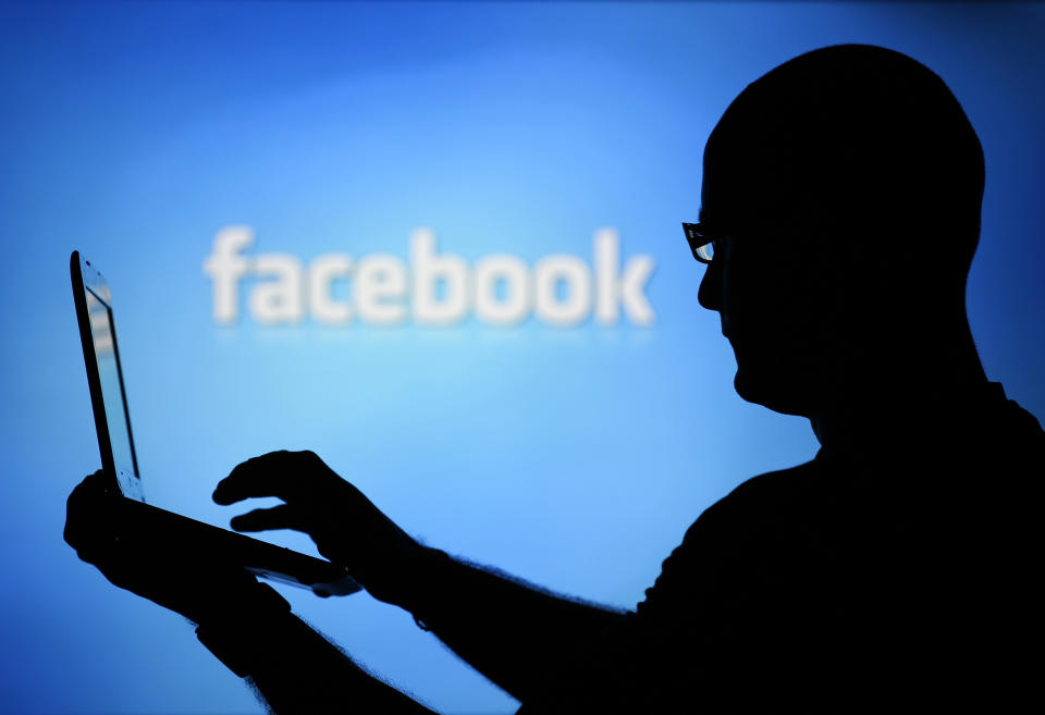 A man is silhouetted against a video screen with an Facebook logo as he poses with an Dell laptop in this photo illustration taken in the central Bosnian town of Zenica, August 14, 2013. REUTERS/Dado Ruvic (BOSNIA AND HERZEGOVINA - Tags: BUSINESS TELECOMS)