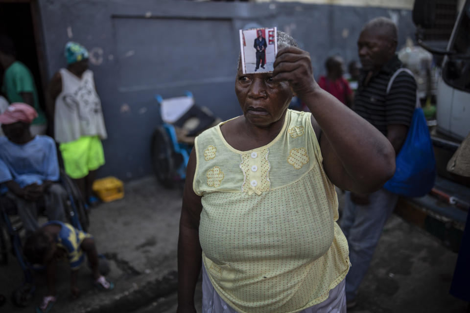 Twice displaced due to the country's escalating violence, Marie Jaquesmal poses with a portrait of her son Michel, who went missing during an assault lead by police, in Port-au-Prince, Haiti, Thursday, Sept. 16, 2021. With 139 houses set fire behind her, she lost track of her 28-year-old son, who is deaf and cannot speak. "I don't know if he is dead or alive, the only thing I saw is that those men were policemen." (AP Photo/Rodrigo Abd)