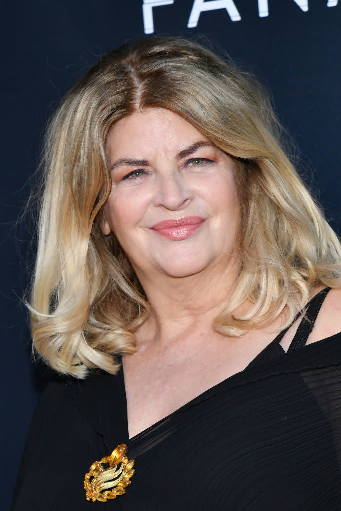 Woman with shoulder-length hair wearing a black off-shoulder dress with a gold brooch