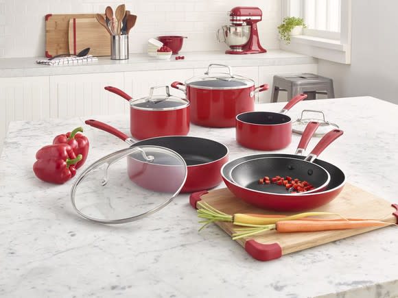 A red KitchenAid cooking set on display with two red peppers, a carrot, and a chopping board on a granite countertop.