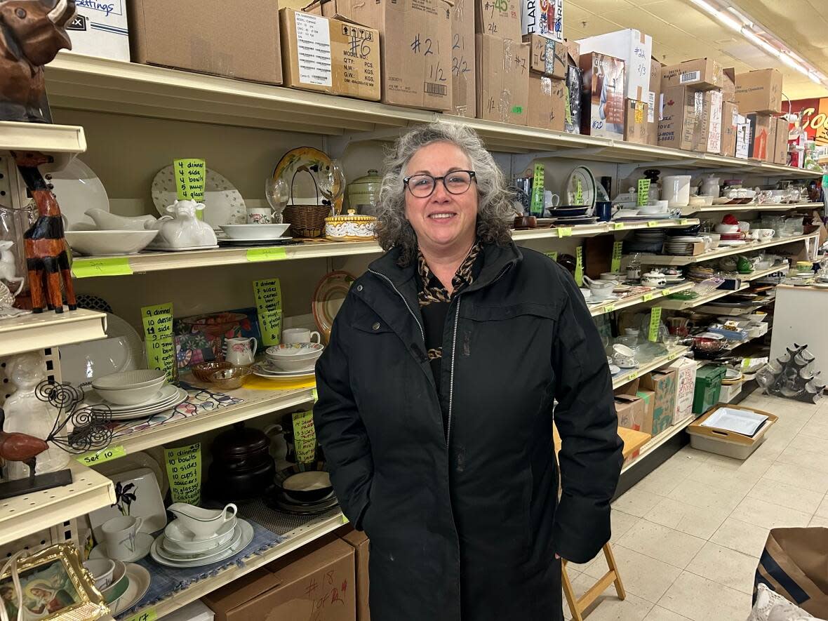 Suzi Shore Sauvé stands in front of dinnerware sets organized and put on for display by volunteers at House to Home. (Laura Glowacki/CBC - image credit)