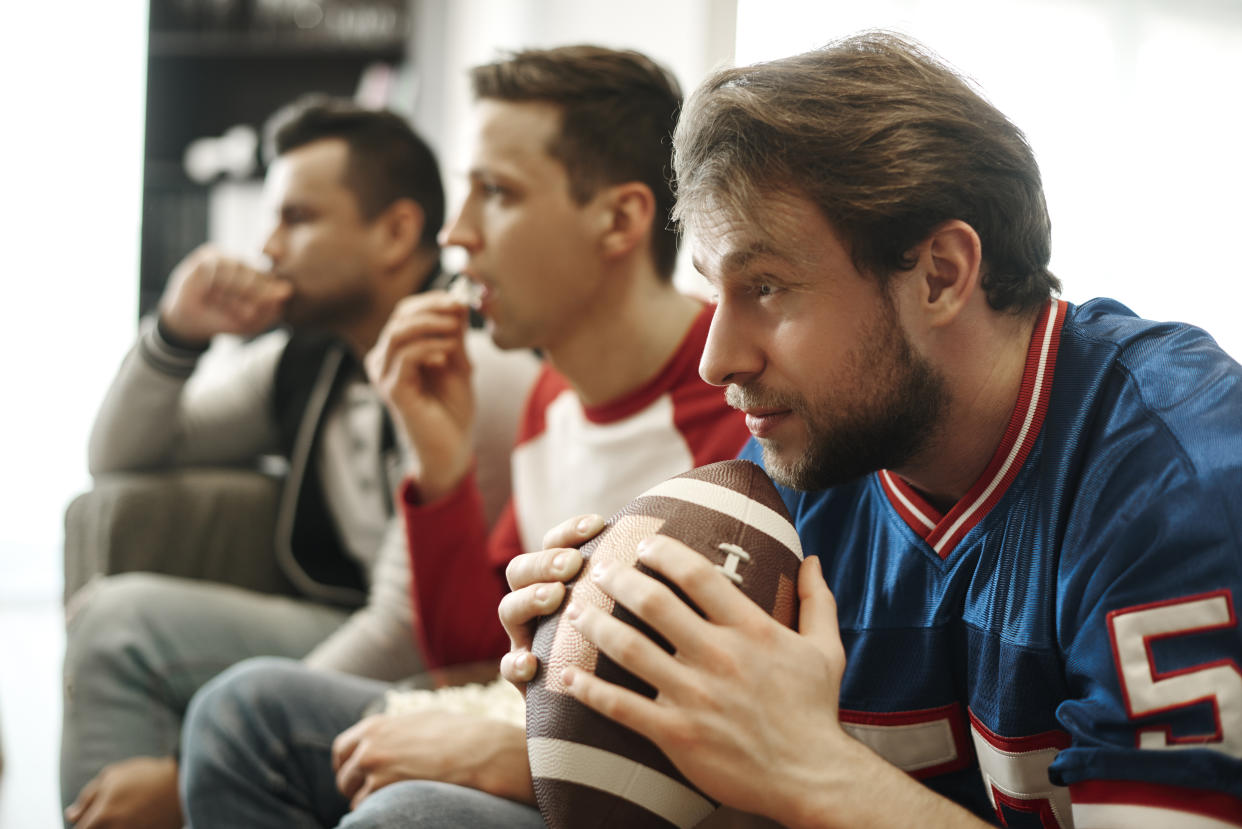 Football fans focused watching a game at home on the couch.