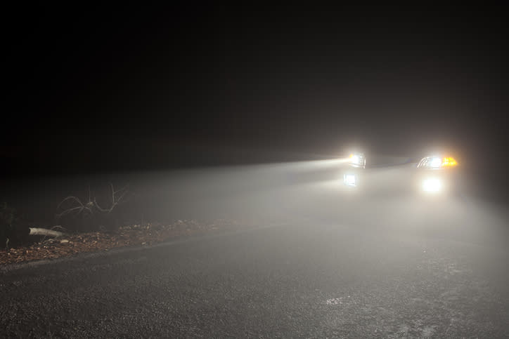 A car with headlights on is driving through a dark, foggy area at night