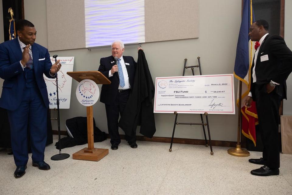 Bud Lafferty, president of the Lafayette Society, unveils a check that will endow a history scholarship at Fayetteville State University, at the society’s annual meeting on March 6, 2022 at SkyView on Hay. FSU Chancellor Darrell Allison applauds on the left. The endowment stems from a years-long partnership between the Lafayette Society and the FSU Black History Scholars Association, which comprised mostly students.