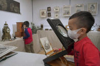 Visitors wearing face masks to protect against the spread of the coronavirus, play a photo viewer, right, and a stereoscope made from France, at an exhibition "A Journey to Europe in 1900", in Hong Kong, Saturday, Feb. 6, 2021. (AP Photo/Kin Cheung)