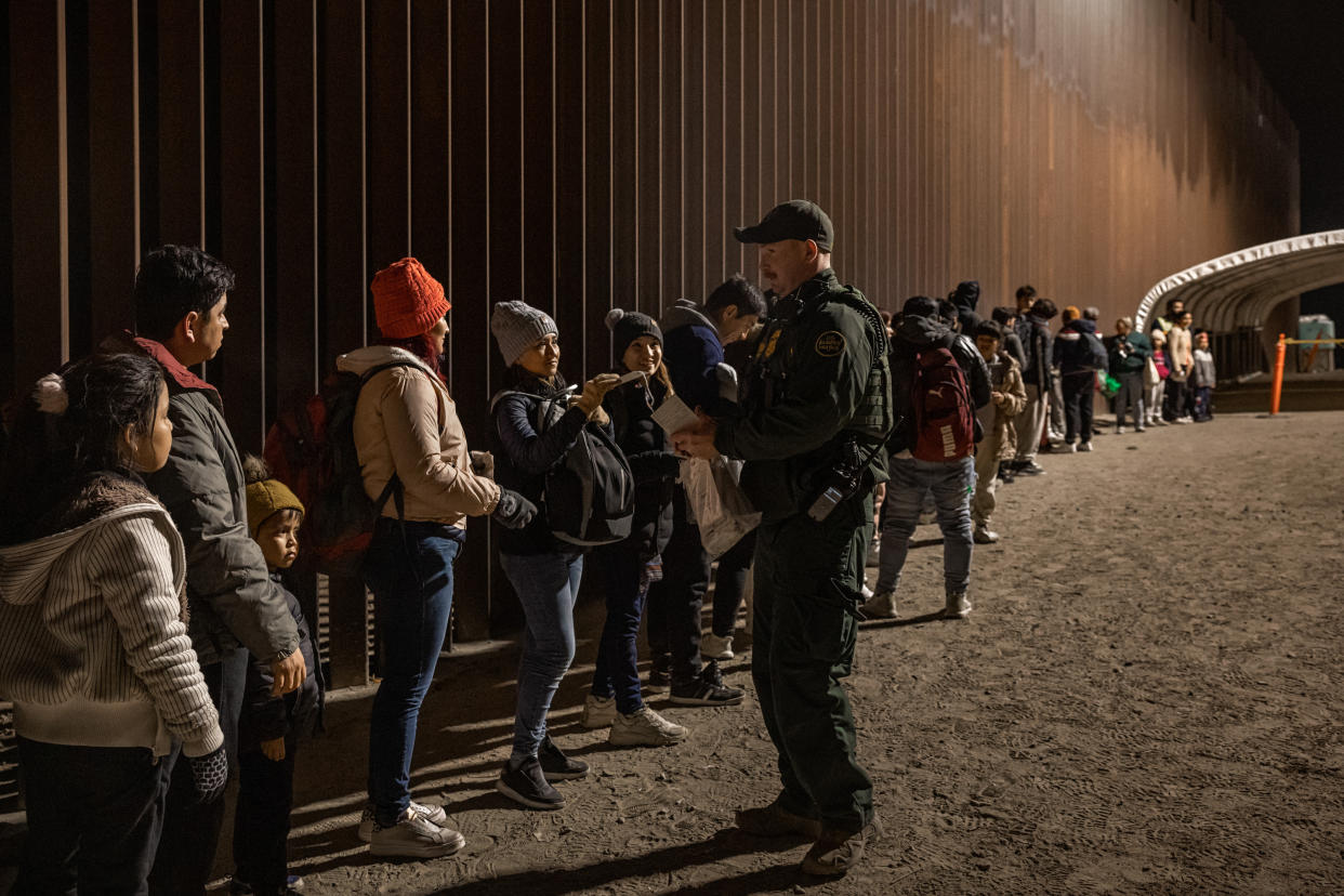 A Border Patrol agent talks to some women in a long line of prospective immigrants.