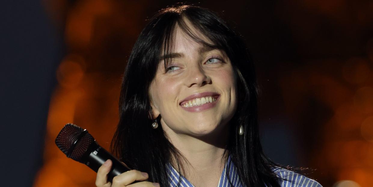 billie eilish in a blue striped shirt and tie holding a microphone