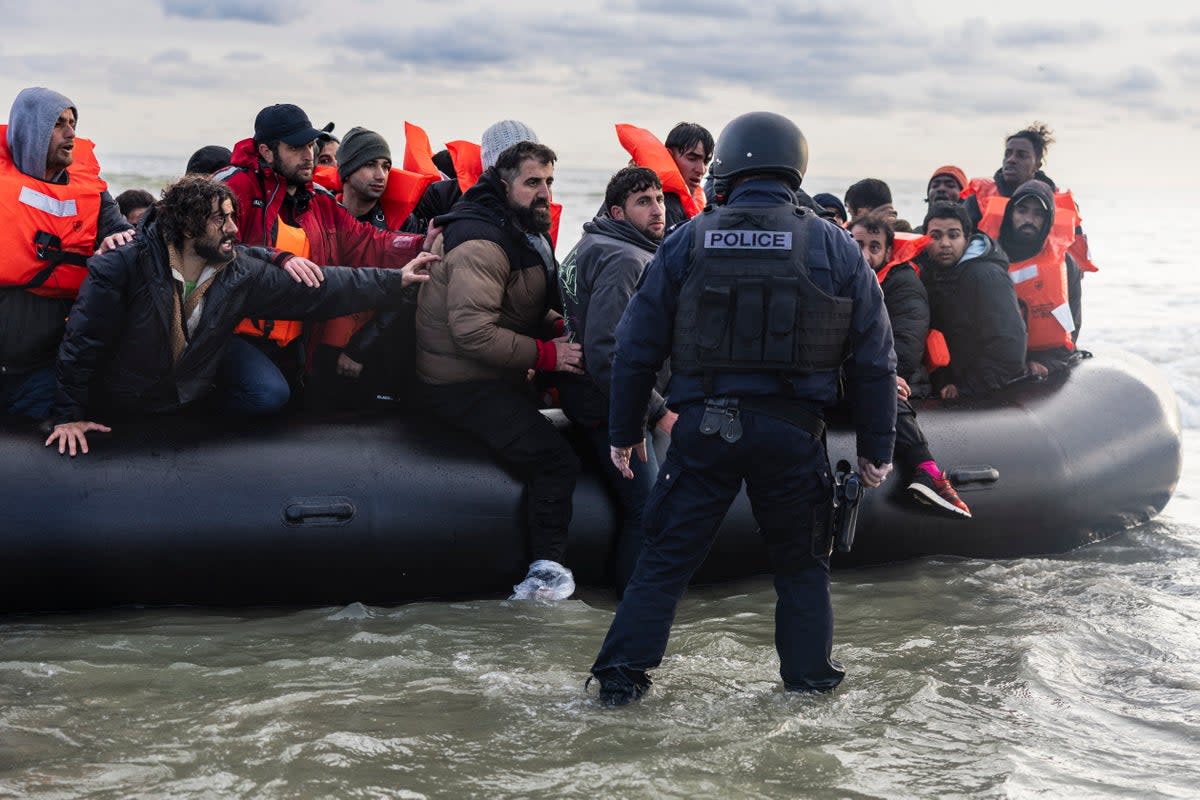 Migrants react as a French police officer stands by ready to puncture the smuggler’s boat to prevent migrants from embarking in an attempt to cross the English Channel (AFP via Getty Images)