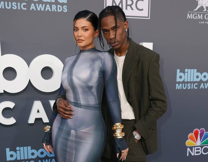 Kylie in a form-fitting dress cuddles with Travis, who's wearing a suit as they pose for photographers on the red carpet