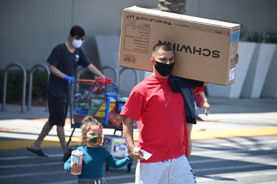 A man wearing a facemask carries a children's bicycle just purchased at Walmart as he walks back to his car, July 22, 2020 in Burbank, California. - New bicycles have been in short supply since early April when bicycle sales surged in response to the coronavirus pandemic. (Photo by Robyn Beck / AFP) (Photo by ROBYN BECK/AFP via Getty Images)