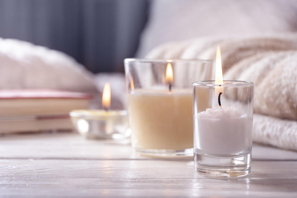 Home interior. Still life with detailes. Several candles on white wooden table in front of bed, the concept of cosiness. Close up.