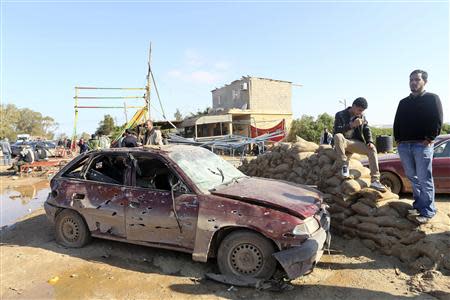 Men look at the scene near a military base in Barsis, some 50 km (30 miles) outside Benghazi, after a suicide bomber detonated a truck packed with explosives at an army checkpoint December 22, 2013. Seven soldiers died in the first such attack since the revolution in Libya's deepening turmoil. REUTERS/Esam Omran Al-Fetori