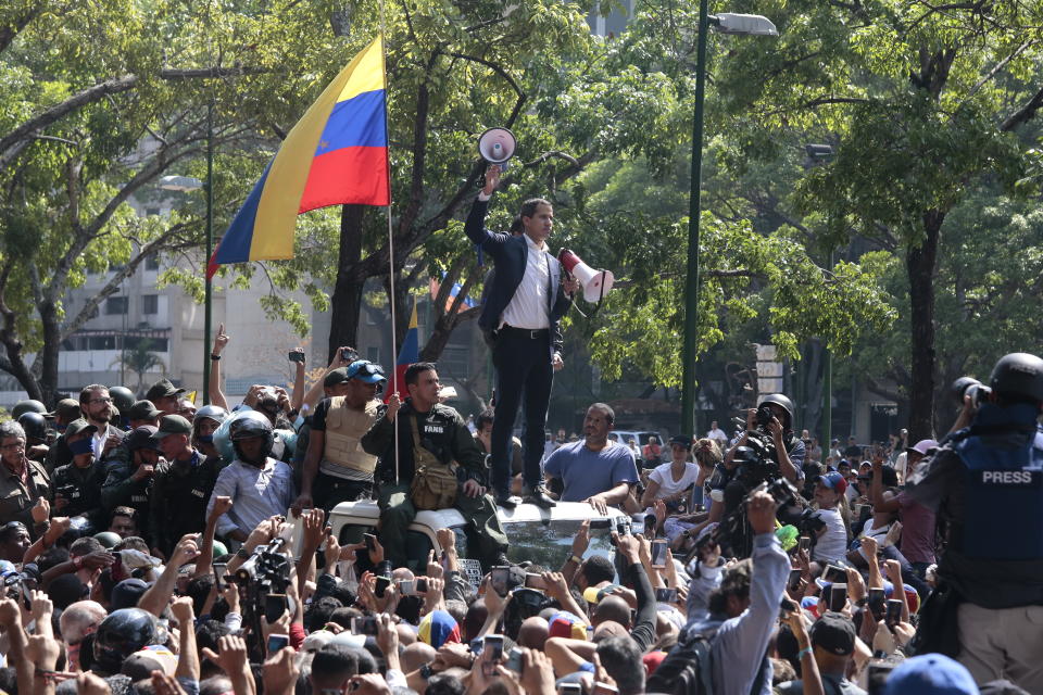 Juan Guaido, Venezuela's parliament leader, stands with two megaphones in his hands surrounded by soldiers and civilians at Plaza Altamira on April 30, 2019 in Caracas, Venezuela. | Rafael Hernandez—picture-alliance/dpa/AP Images