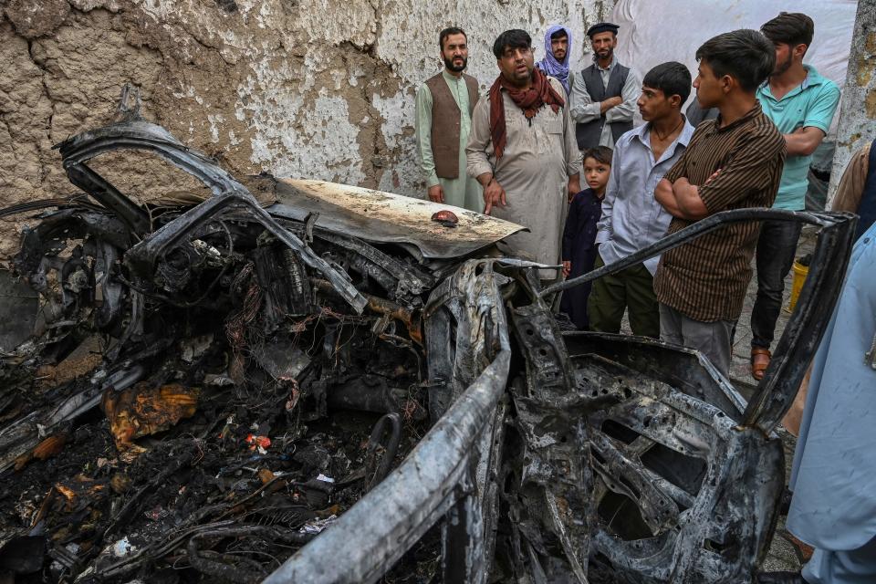 Afghan residents and family members of the victims gather next to a damaged vehicle inside a house, day after a US drone airstrike in Kabul on 30 August, 2021.  ((Photo by WAKIL KOHSAR / AFP))