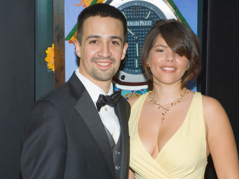 Lin-Manuel Miranda smiles in a tuxedo next to his wife Vanessa Nadal dressed in a yellow gown