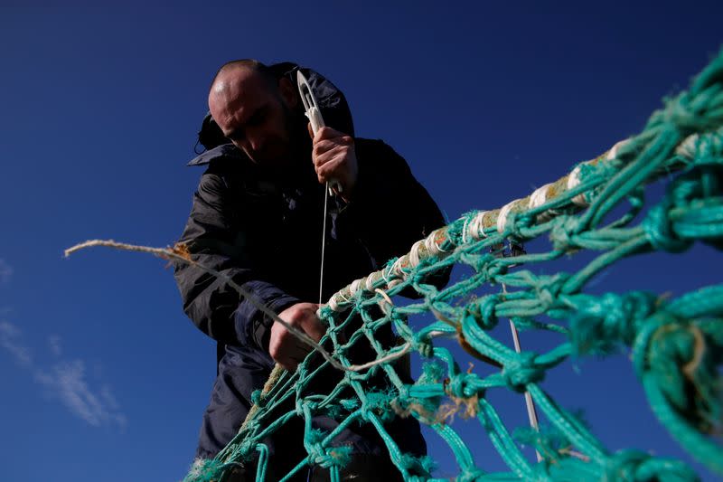 A fisherman repairs a fishing net on the dock of the port in Boulogne-sur-Mer