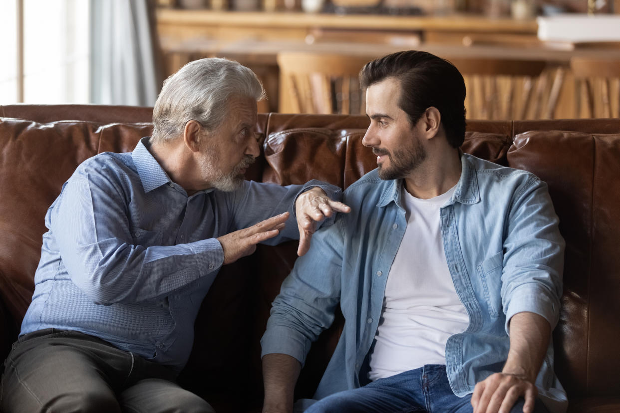 Grown up adult son visiting elderly father for spending leisure time together. Old and young men meeting, sitting and talking on couch at home. Two family generations, relations concept.