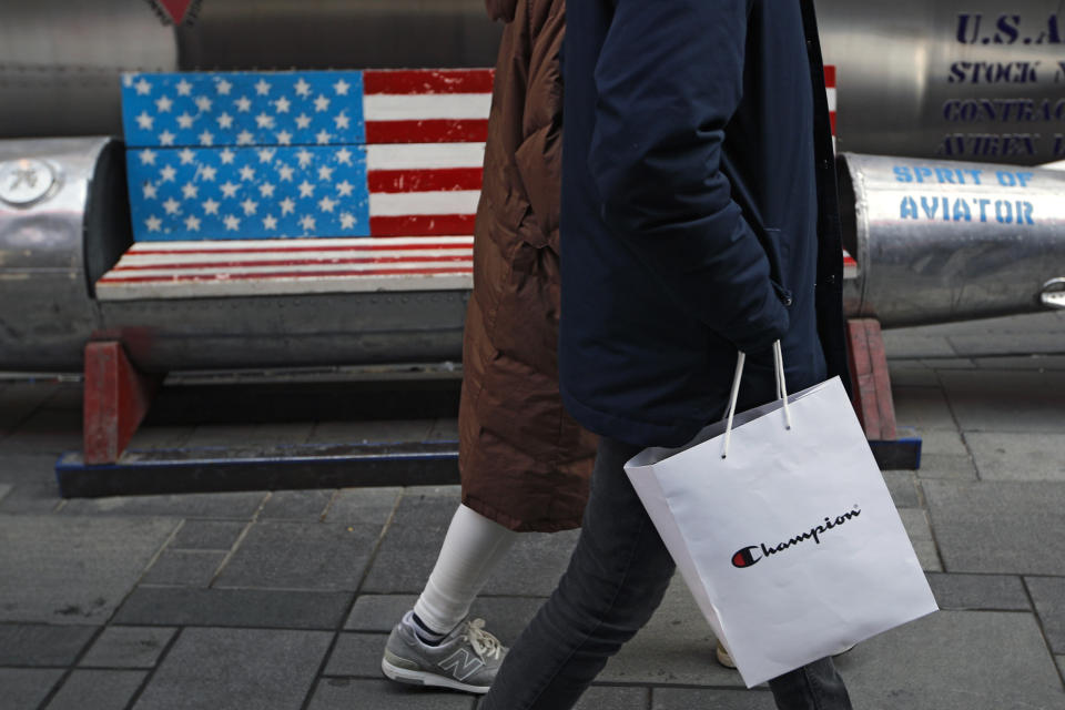 A couple carries a paper bag containing goods purchased from American brand Champion past a bench painted with the U.S. flag at the capital city's popular shopping mall in Beijing, Wednesday, Feb. 13, 2019. U.S. and Chinese negotiators are meeting this week for their final trade talks before President Donald Trump decides whether to escalate a dispute over technology with a March 2 tariff hike on $200 billion of imports from China. (AP Photo/Andy Wong)