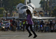 A young woman runs across the street in front of the space shuttle Endeavour as it is slowly moved down Crenshaw Blvd., Saturday, Oct.13, 2012, in Los Angeles. The shuttle is on its last mission — a 12-mile creep through city streets. It will move past an eclectic mix of strip malls, mom-and-pop shops, tidy lawns and faded apartment buildings. Its final destination: California Science Center in South Los Angeles where it will be put on display. (AP Photo/Mark J. Terrill)