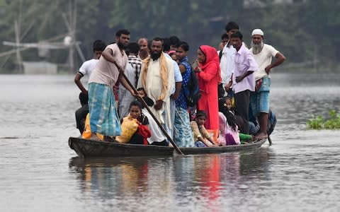 Indian villagers travel by boat through floodwaters in Morigoan district, in India's northeastern state of Assam.  - Credit: Biju Boro/AFP