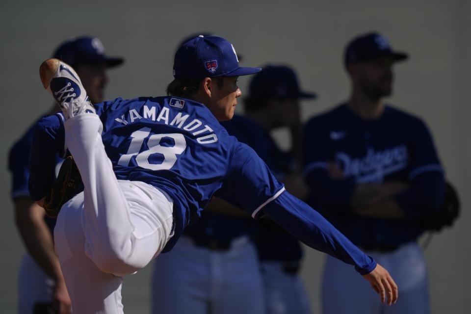 Dodgers pitcher Yoshinobu Yamamoto (18) follows through as teammates watch from the shade during a workout Friday in Phoenix.