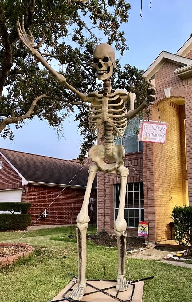 A skeleton in front of a house with a "Do your homework" sign hanging off it
