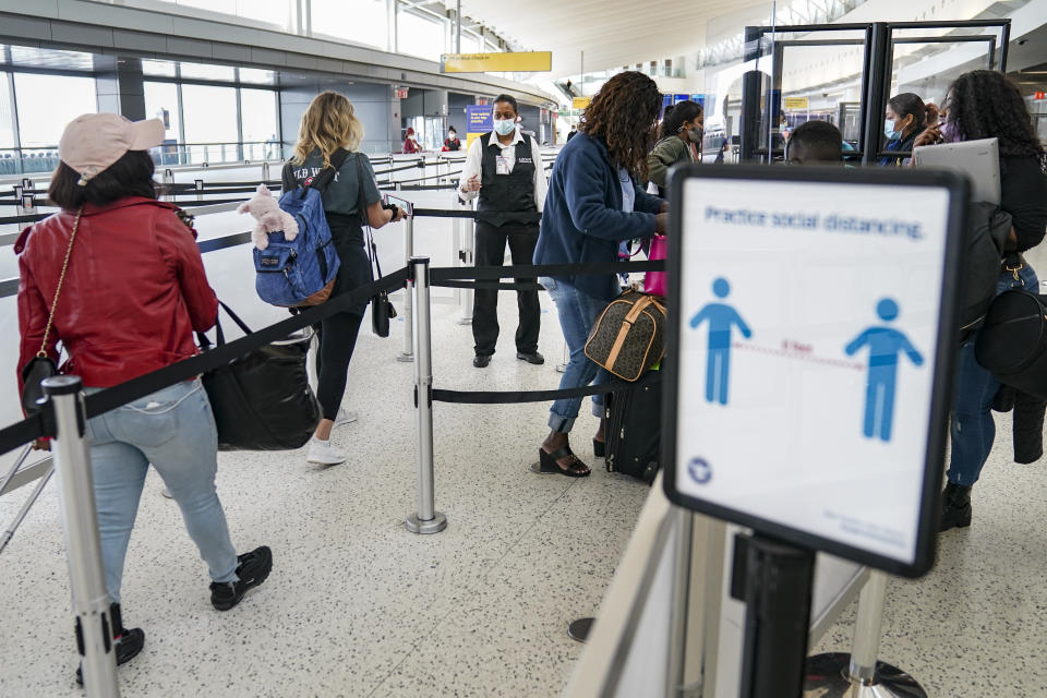 FILE - In this Oct. 20, 2020, file photo, transportation Security Administration personnel and travelers observe COVID-19 transmission prevention protocols at John F. Kennedy International Airport in the Queens borough of New York. The United States is approaching a record for the number of new daily coronavirus cases in the latest ominous sign about the disease's grip on the nation. (AP Photo/John Minchillo, File)