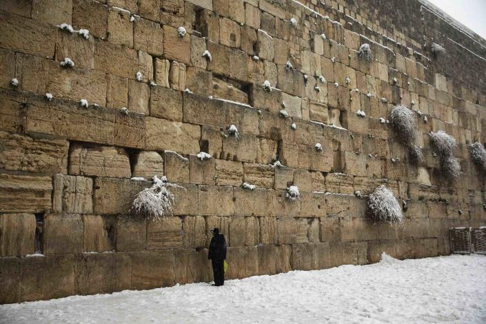 A man prays in the snow at the Western Wall, Judaism's holiest prayer site, in Jerusalem's Old City February 20, 2015. Snow covered Jerusalem and mountainous areas of Israel early Friday morning and the education ministry closed schools for the day. (REUTERS/Ronen Zvulun)