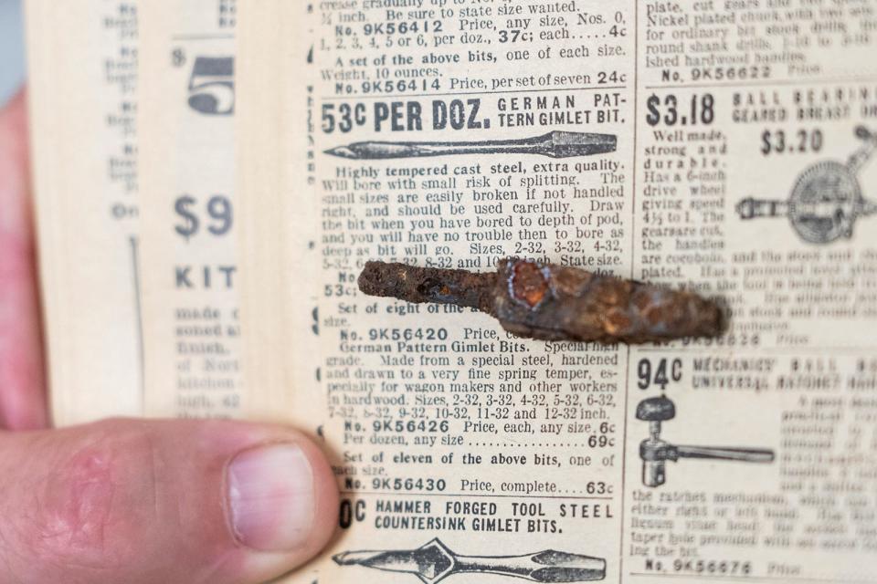 Blacksmith Kelly Kring matches an old drill bit to an advertisement for a drill bit in a catalogue as he looks at artifacts from Tom Cook's blacksmith shop.