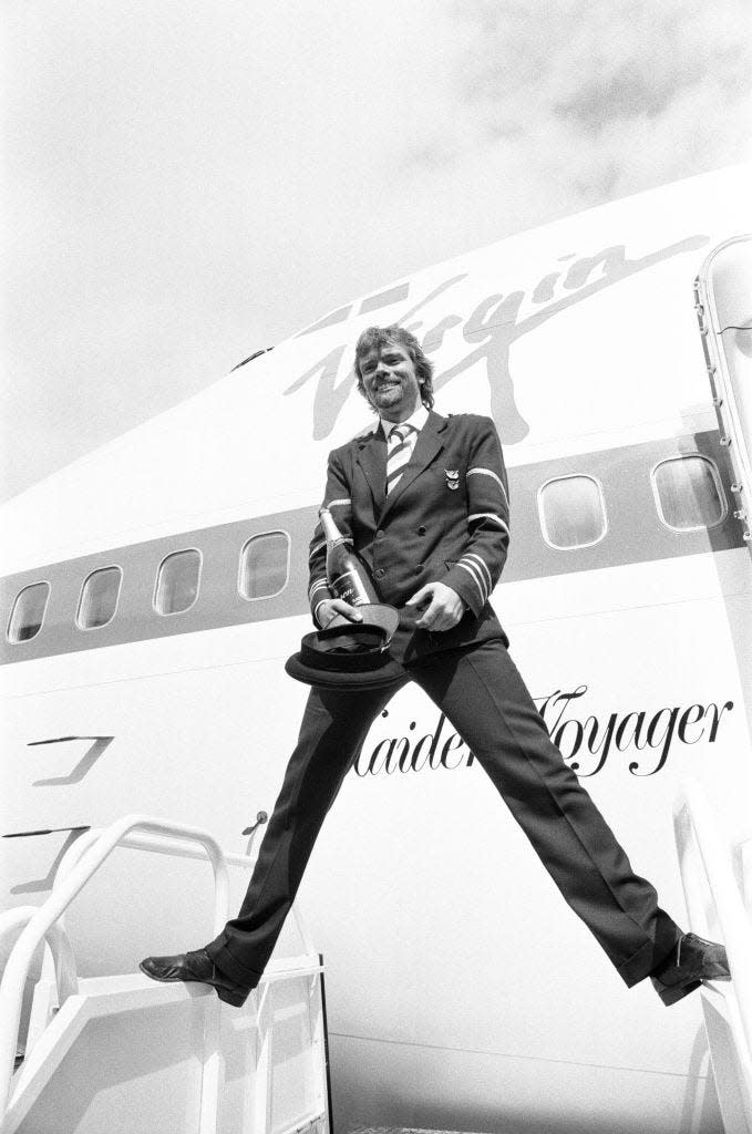 Richard Branson here dressed as a Virgin Atlantic pilot with a bottle of champagne, posing for the press in front of Virgin Atlantic's first Boeing 747 Maiden Voyager before the airline's inaugural flight. 21st June 1984.