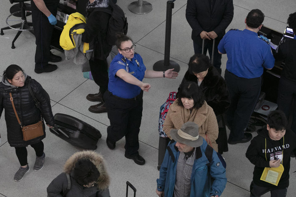 FILE- In this Jan. 7, 2019, file photo a TSA agent, center, directs passengers through a security checkpoint at New York's John F. Kennedy International Airport. The strain of a 34-day partial government shutdown is weighing on the nation's air-travel system, both the federal workers who make it go and the airlines that depend on them. Unions that represent air traffic controllers, flight attendants and pilots are growing concerned about safety with the shutdown well into its fifth week. (AP Photo/Mark Lennihan, File)