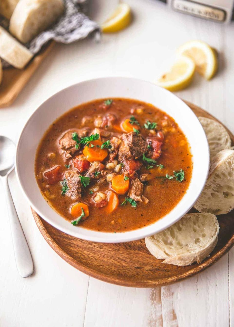 slow cooker beef and barley soup in bowl with bread slices on side