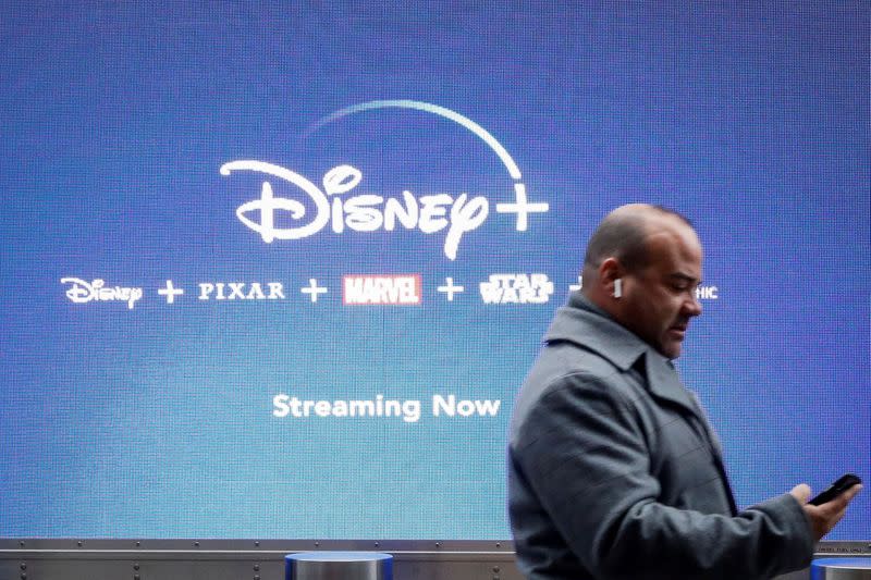 FILE PHOTO: A man looks at his phone as he passes by a screen advertising Walt Disney's streaming service Disney+ in New York, USA