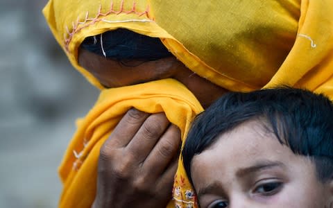 a Pakistani woman cries in her scarf as she holds her HIV infected child outside a house at Wasayo village in Rato Dero - Credit: AFP