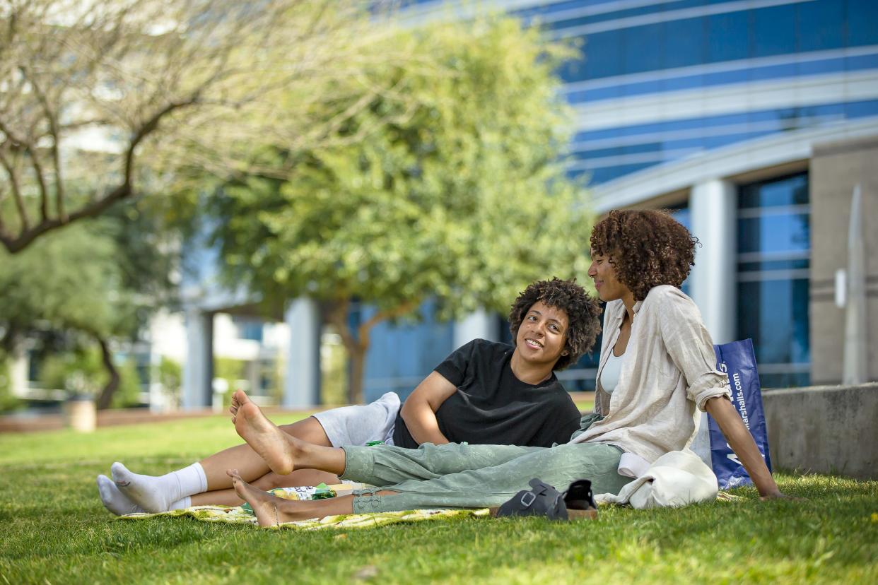 Whitney Blue and Stephanie Lamarche lounge in the shade on a grassy area at Tempe Beach Park on March 25, 2022.