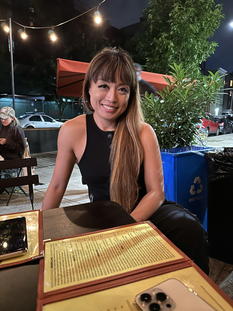 <p>A photo from the iPhone 14 Pro's rear main camera of a woman sitting at a table in an outdoor restaurant.</p>
