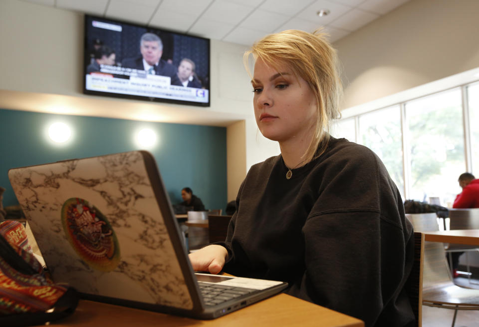 Catherine Mitchell, a biology major at California State University, Sacramento, works on her laptop during a break between classes, as William Taylor, the top U.S. diplomat in the Ukraine, is seen on television testifying before the House Intelligence Committee, in Sacramento, Calif., Wednesday, Nov. 13, 2019. The committee held its first public impeachment hearing of President Donald Trump's efforts to tie U.S. aid for Ukraine to investigations of his political opponents. (AP Photo/Rich Pedroncelli)