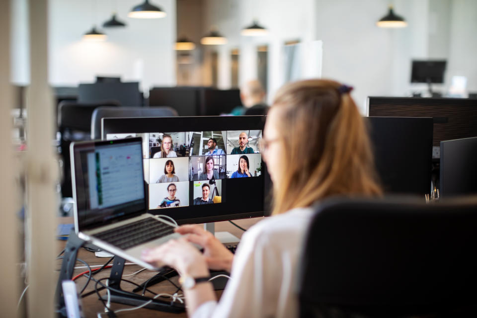 Businesswoman working on her laptop and having a video conference at her work desk. Rear view of a woman discussing work on video call with team members. Back to work post corona virus pandemic lockdown.