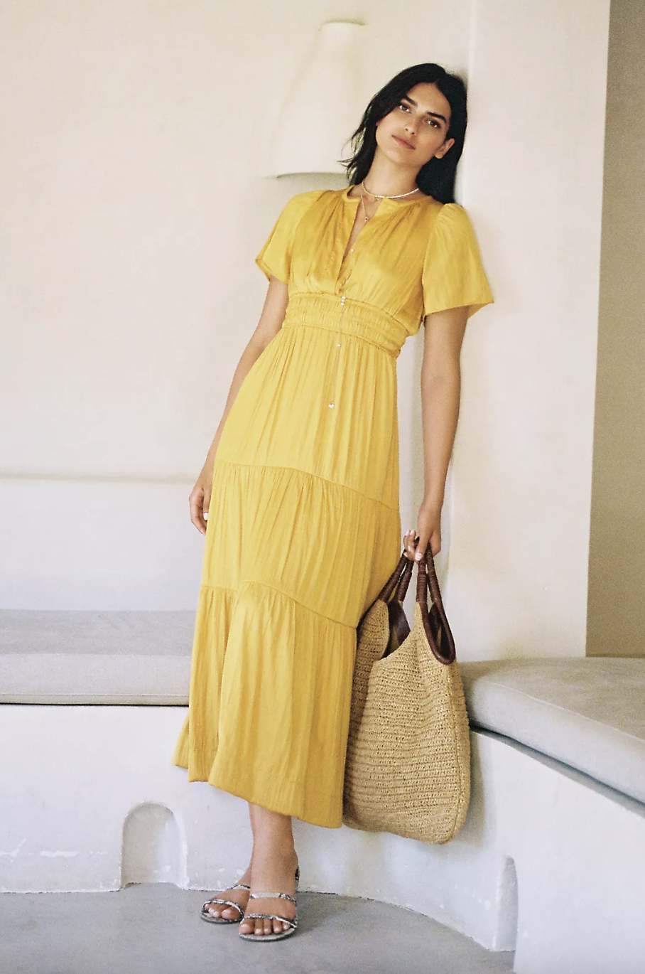 model with dark hair leaning against wall holding rattan bag wearing yellow maxi dress, The Somerset Maxi Dress in mango (Photo via Anthropologie)