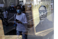 Protesters are reflected in a store window where a portrait of George Floyd is displayed in Manhattan, New York, Monday, June 1, 2020. New York City imposed an 11 p.m. curfew Monday as the nation's biggest city tried to head off another night of destruction erupting amid protests over George Floyd's death. (AP Photo/Seth Wenig)