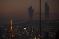 Silhouetted against the warm sunset skyline and the illuminated Tokyo Tower, visitors are reflected on the glass walls of a rooftop observation deck Thursday, Jan. 21, 2021, in Tokyo. (AP Photo/Kiichiro Sato)