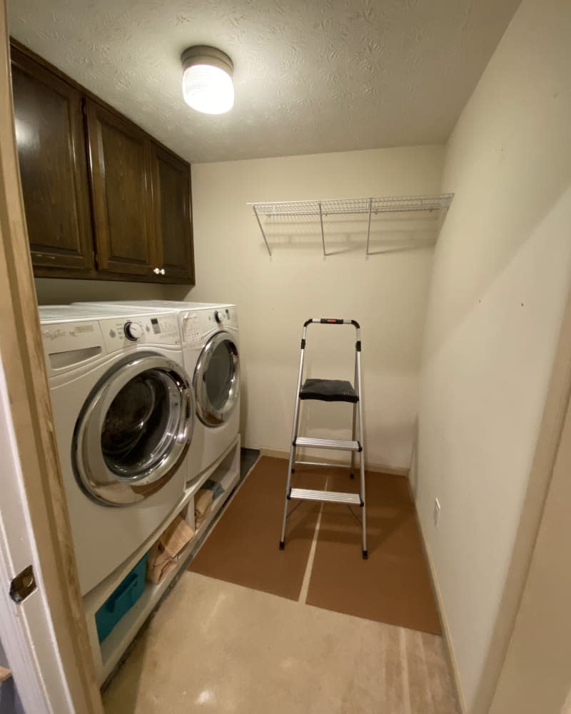 Dark wood cabinets above washer and dryer, white floating shelf with ladder underneath