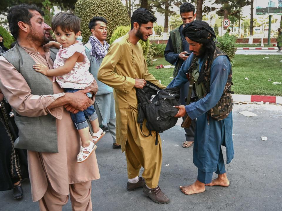 A Taliban fighter (R) searches the bags of people coming out of the Kabul airport in Kabul on August 16, 2021, after a stunningly swift end to Afghanistan's 20-year war, as thousands of people mobbed the city's airport trying to flee the group's feared hardline brand of Islamist rule. (Wakil Kohsar/AFP via Getty Images)