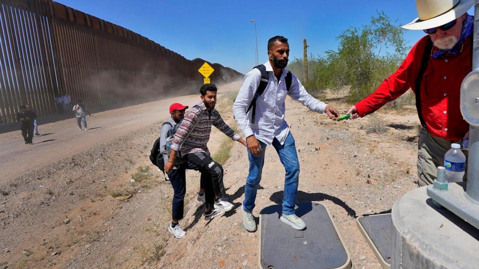 PHOTO: Tom Wingo of Samaritans Without Borders, right, gives snacks and bottles of waters to a group of migrants claiming to be from India, who just crossed the border wall, Aug. 29, 2023, in Organ Pipe Cactus National Monument near Lukeville, Ariz. (Matt York/AP, FILE)