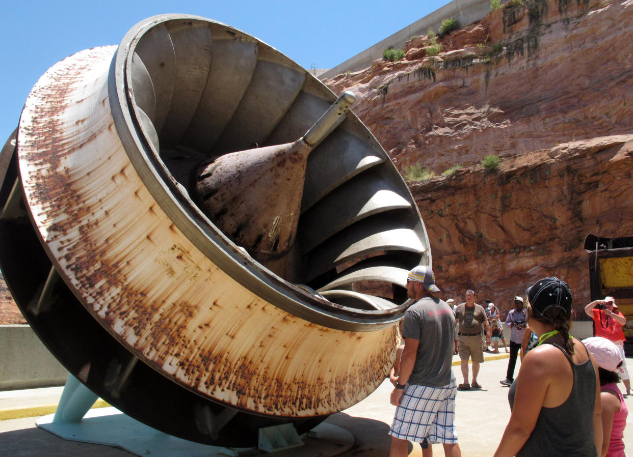 In this Sunday, June 21, 2015 photo tourists look up at an old turbine runner during a tour of Glen Canyon Dam in Page, Ariz. The U.S. Bureau of Reclamation is wrapping up a project to replace the eight turbines that produce electricity at the dam. (AP Photo/Felicia Fonseca)